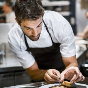 Mid adult male cook garnishing food. Chef is preparing dish in commercial kitchen. He is working in restaurant.